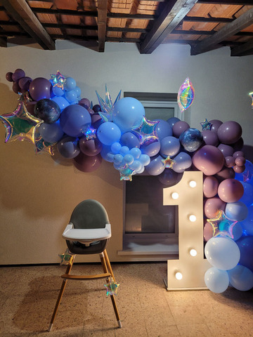 Chaise haute devant une arche organique en ballon, chiffre géant et étoiles suspendues