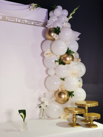 Une arche de ballons blancs et dorés rappelant la pureté de l'Olympe agrémentée de fleurs délicates
