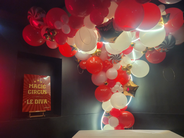 Vue d'ensemble de la pièce maitresse de la décoration : l'arche de ballons illuminée par un néon. Elle est ornée de détails dorés comme des cercles rappelant les cerceaux des artistes.