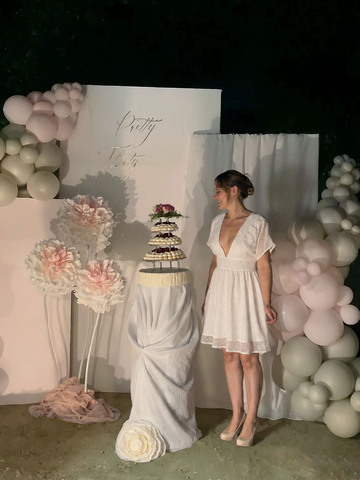 Pavlova Gourmande et toquée sur plusieurs étage trônant sur un socle drapé complétant la scénographie. Clémy, la décoratrice, se tient devant sa création, prête à célébrer son anniversaire.
